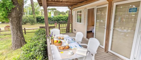 A covered outdoor seating area with a table, chairs, and a view of the surrounding garden.
