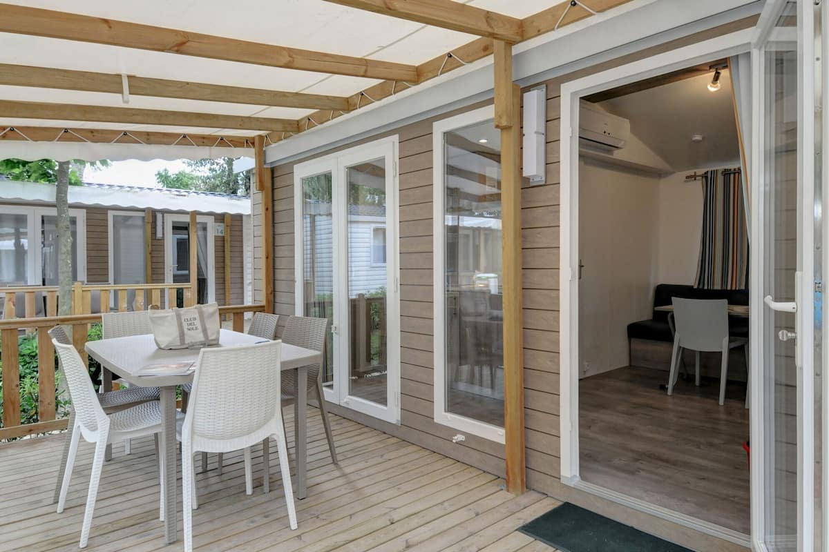 A covered outdoor area with a table and chairs, a sliding glass door leading to an interior space, and a wooden deck.