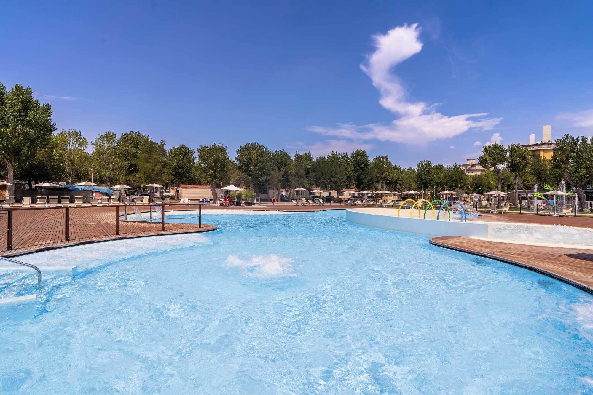 A swimming pool with a wooden deck, lounge chairs, and umbrellas.