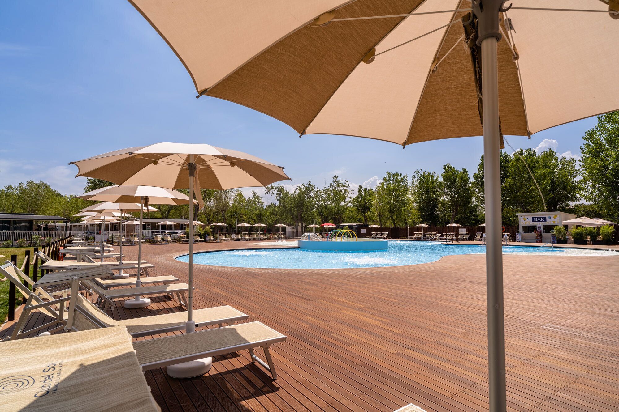 Zona junto a la piscina con sillones de descanso y sombrillas, un bar y una piscina.
