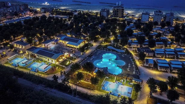 Vista aerea di un resort con piscine, spiaggia e un porto turistico.