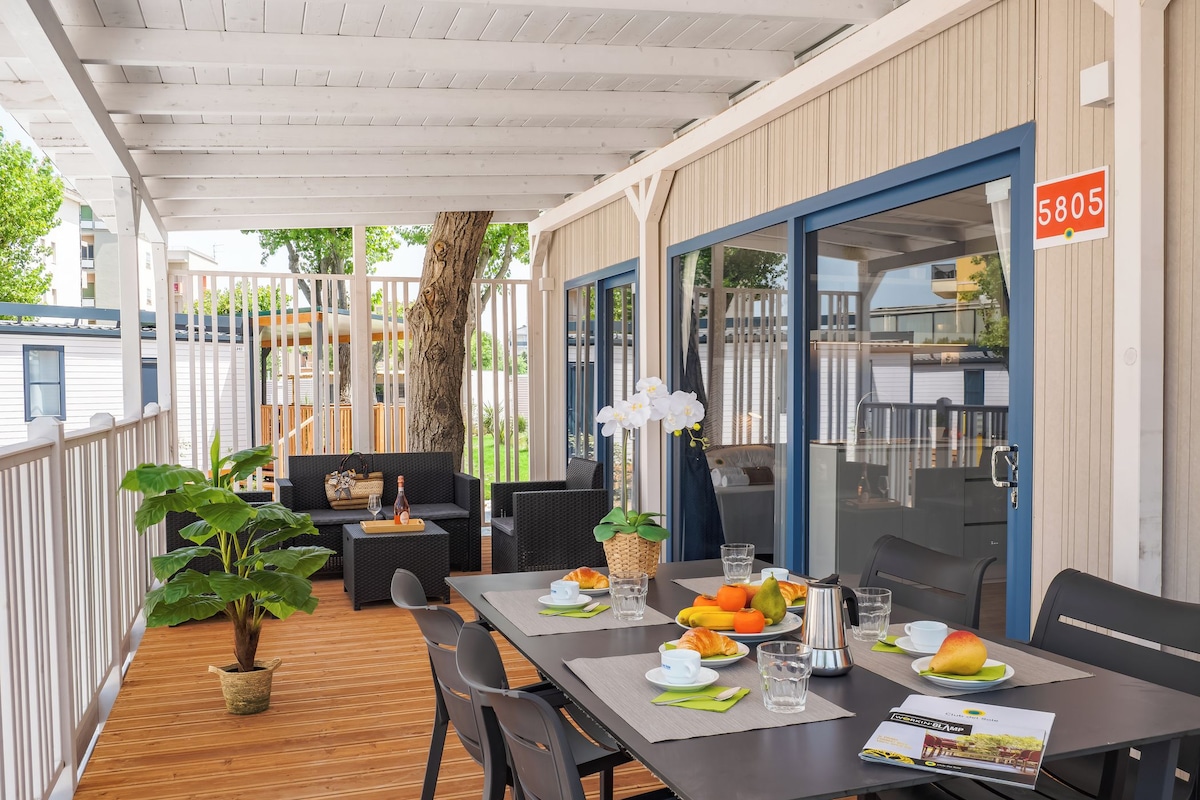 A covered outdoor dining area with a table set for breakfast, including fruits, pastries, and beverages.