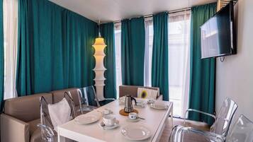 Un coin repas avec une table dressée pour quatre personnes, des chaises transparentes, une cafetière et un téléviseur fixé au mur.