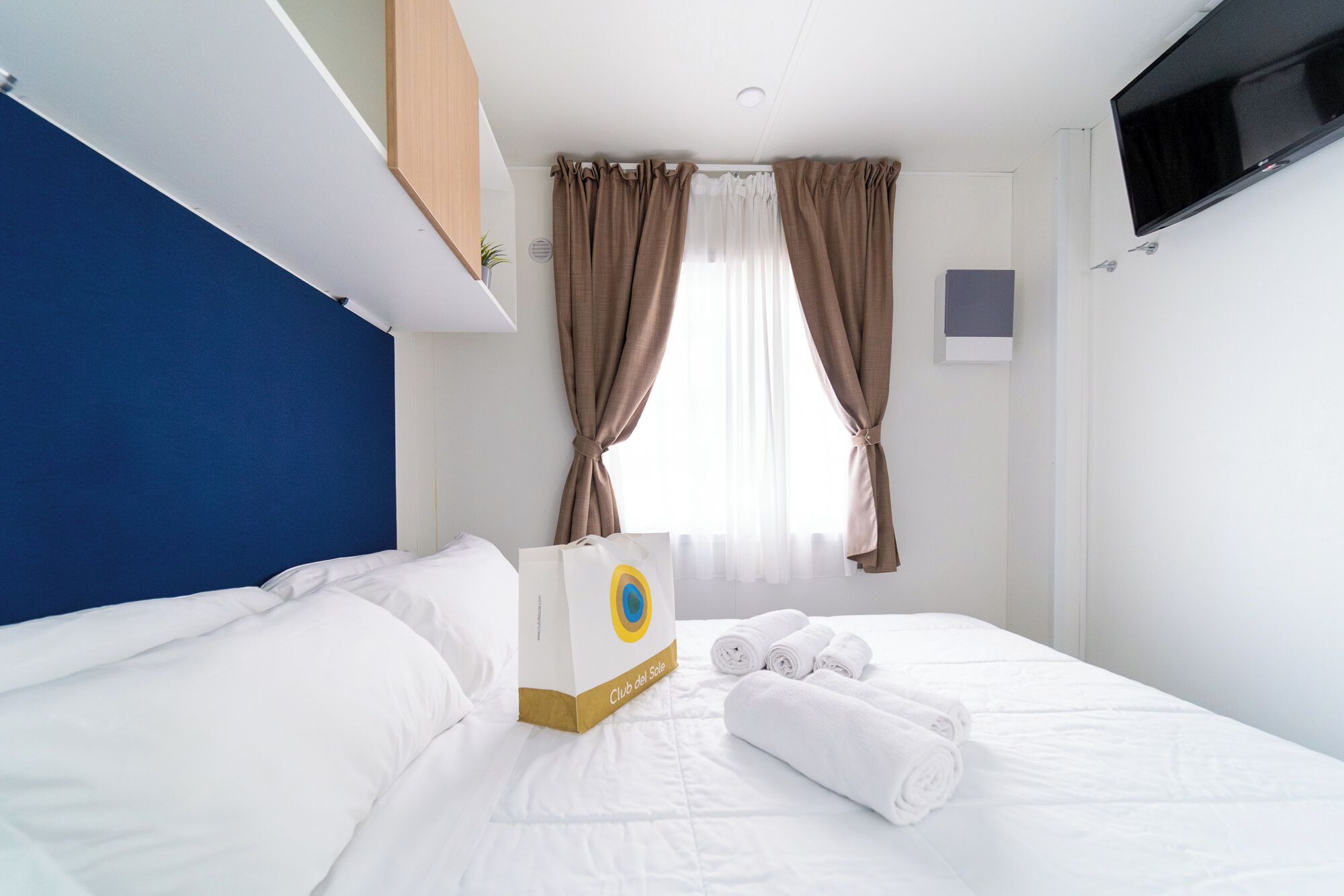 A hotel room with a bed, a TV mounted on the wall, and a window with curtains.