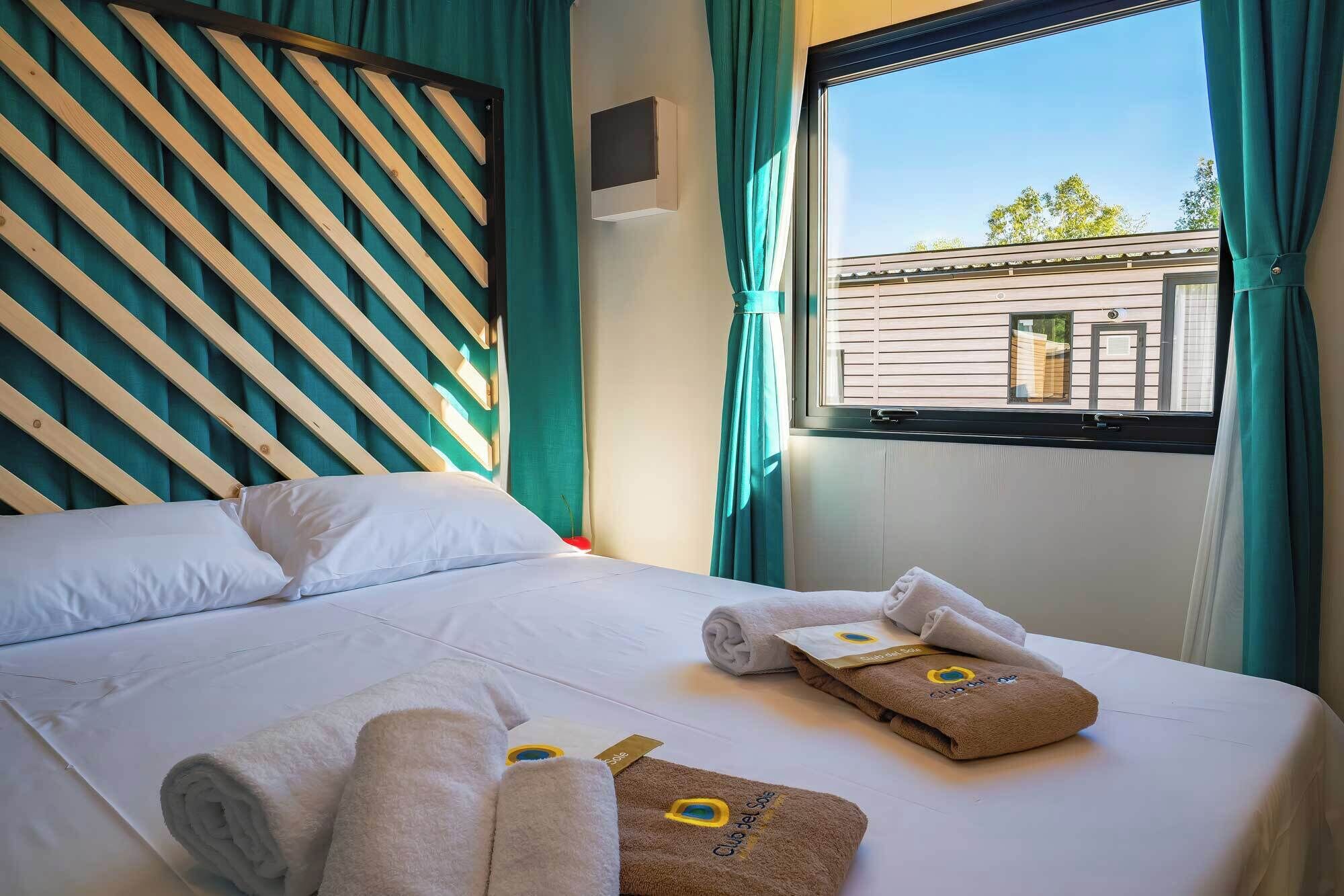 A hotel room with a bed, a window with curtains, and a view of the outside.