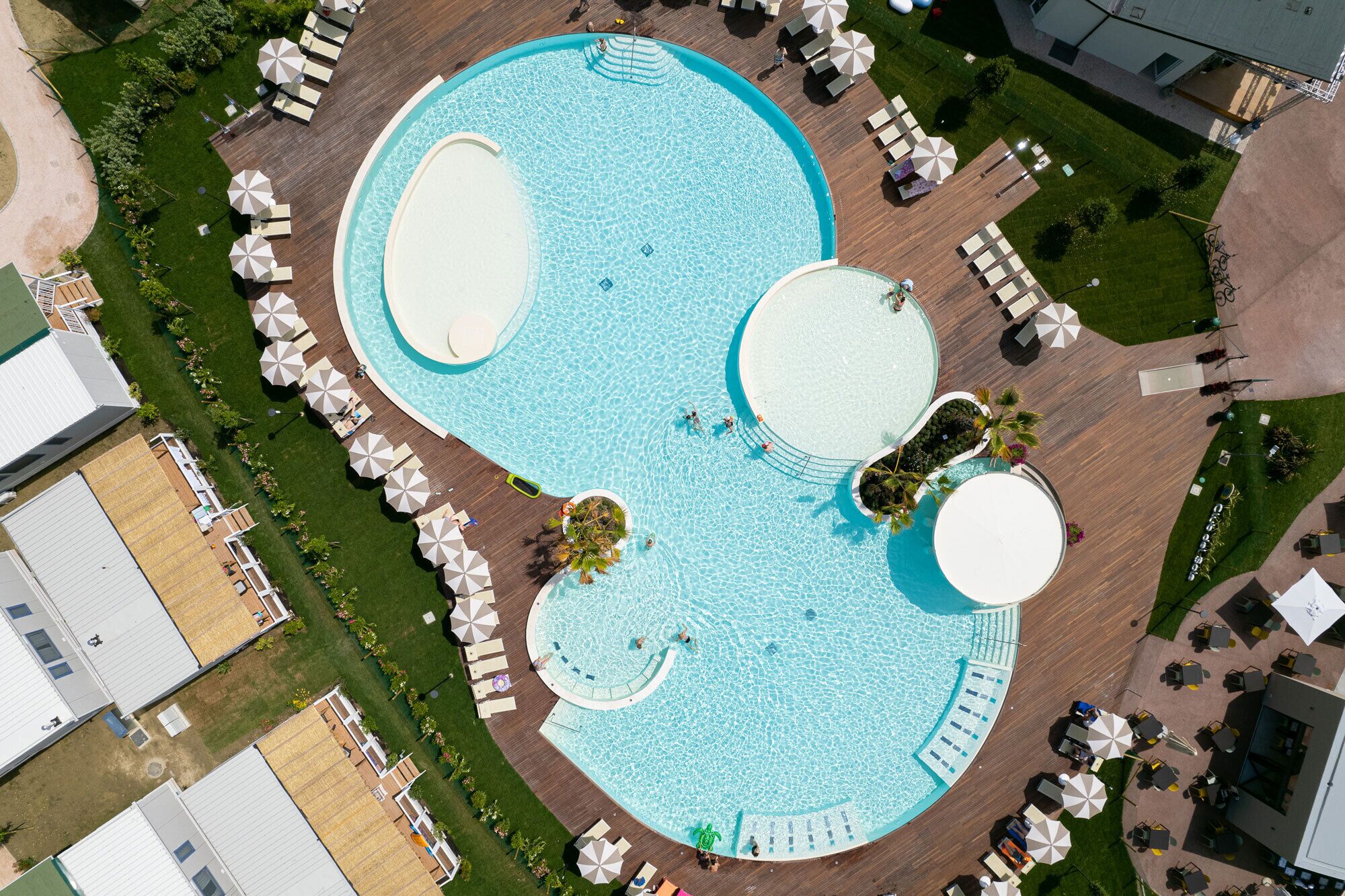 Vista aèria d'una piscina amb diverses zones, envoltada d'espais de relaxació amb ombrelles i gandules.