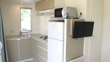 Una cucina compatta con forno a microonde, frigorifero e una piccola TV.