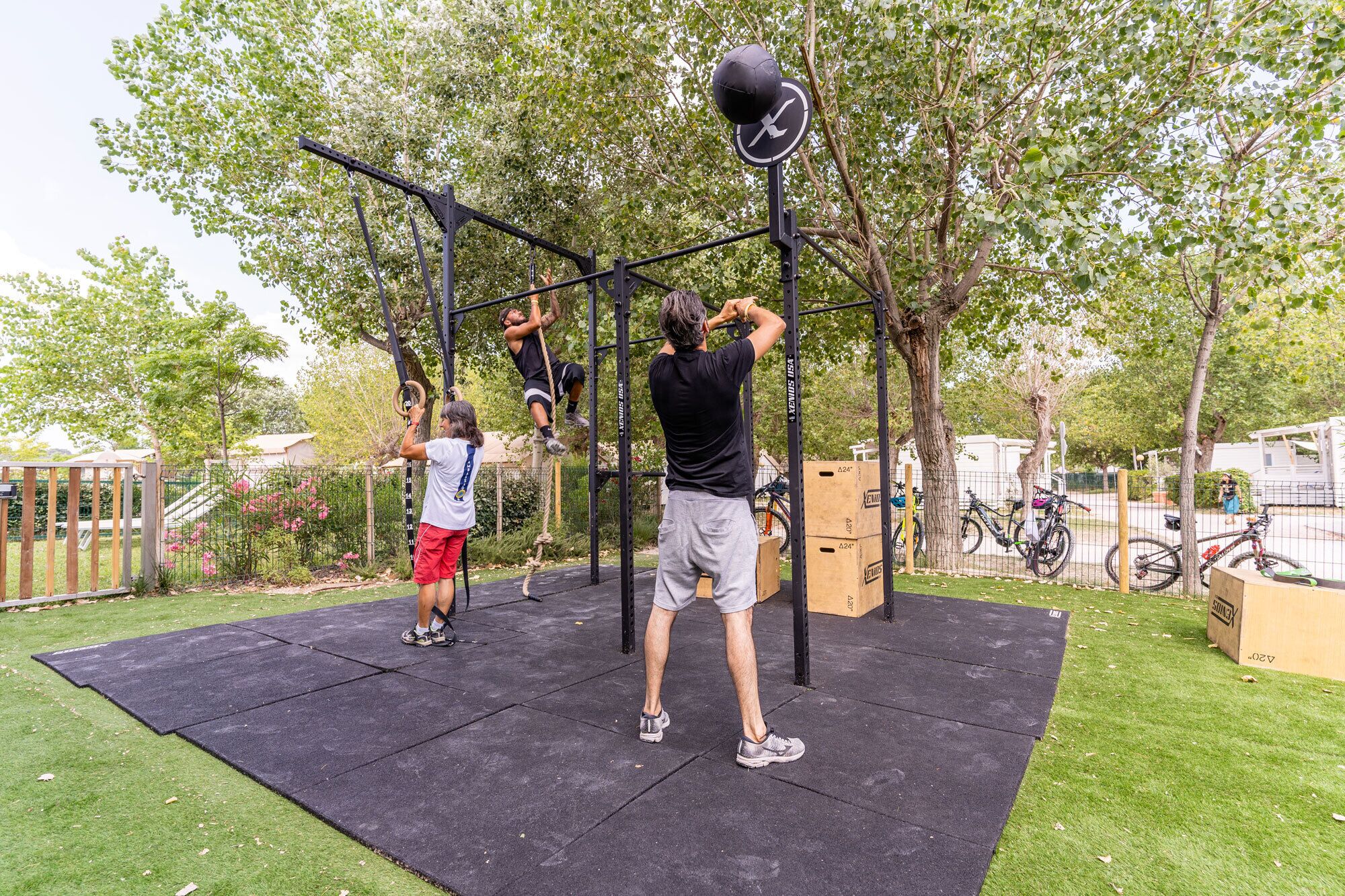 Une salle de sport en plein air équipée de divers appareils, avec un tapis noir et des arbres en arrière-plan.