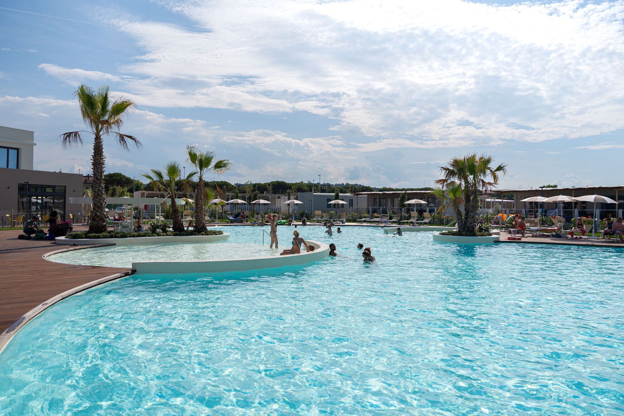 Una grande piscina all'aperto con palme, sdraio e ombrelloni.