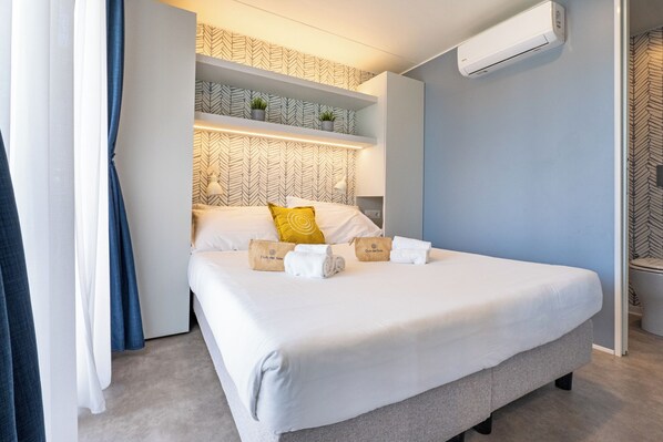 Una habitación de hotel moderna con una cama, aire acondicionado de pared y papel tapiz estampado.