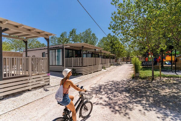 Una mujer pedaleando en bicicleta por un camino de grava, una cerca de madera y un edificio con grandes ventanales.