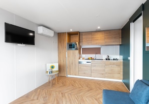 A modern kitchen with wooden cabinets, a microwave, and a flat-screen TV mounted on the wall.