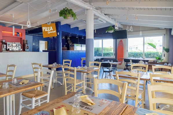 A restaurant interior with multiple tables and chairs, a visible pizza sign, and a coffee machine.