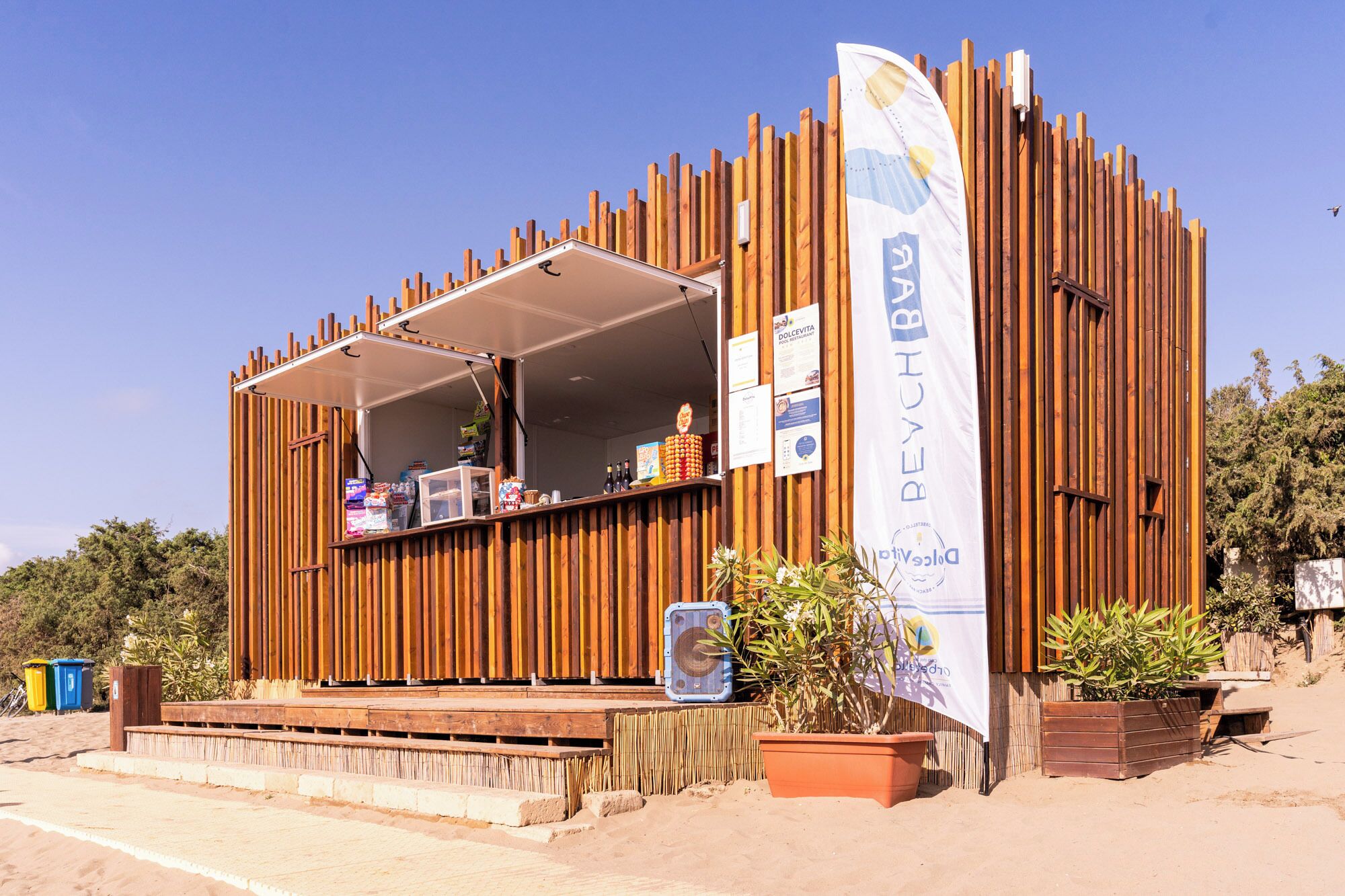 Una estructura de madera con un toldo blanco, un letrero y una planta en maceta.