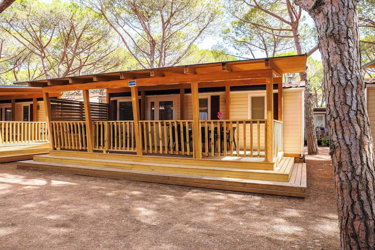 Une cabane en bois dotée d’un porche abrité, d’un coin repas et d’une porte bien visible.