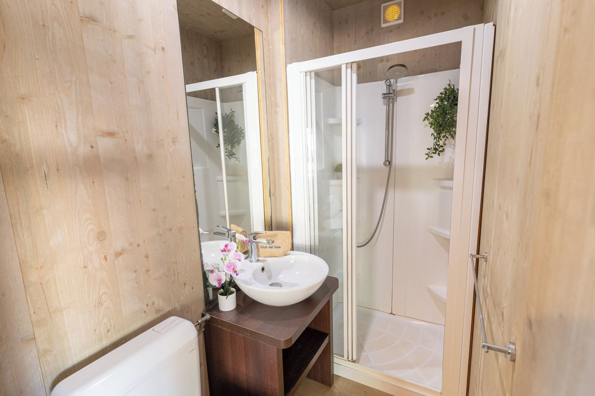 Une salle de bain avec un mur en bois, un lavabo blanc, une cabine de douche en verre et des toilettes.