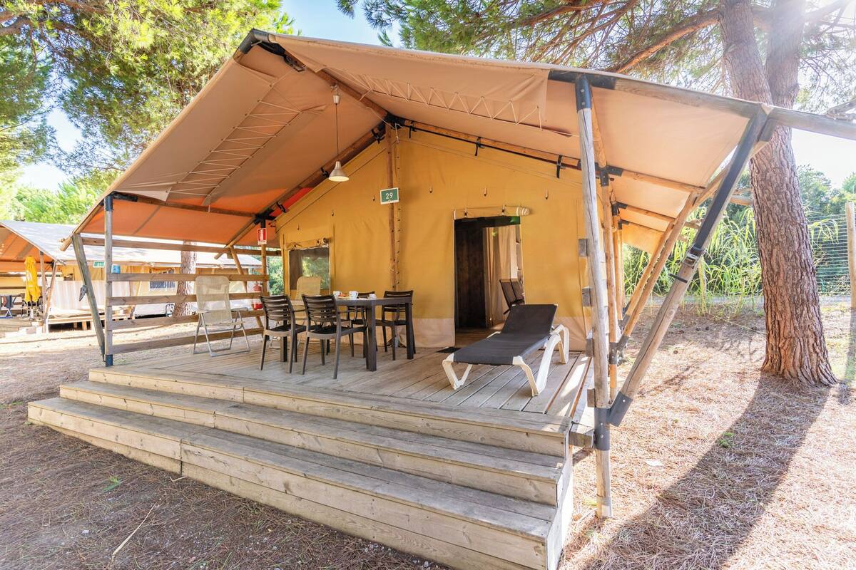 Un espace extérieur aménagé avec une tente, une terrasse en bois, une table avec des chaises et un fauteuil de relaxation.