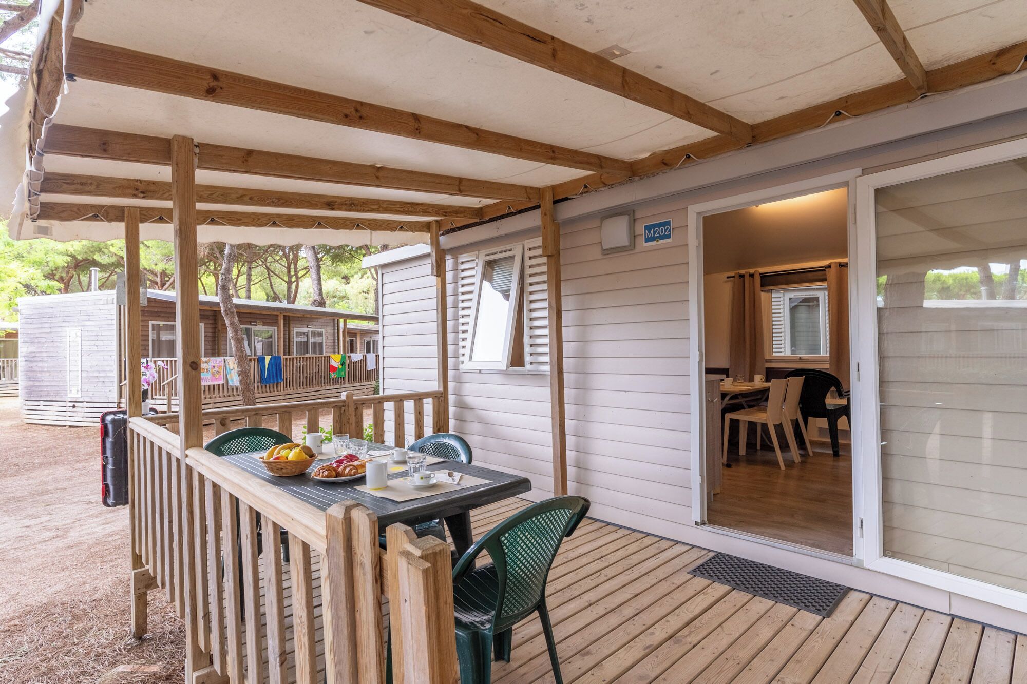A covered outdoor area with a table and chairs, a wooden deck, and a view of a house with a sliding door.