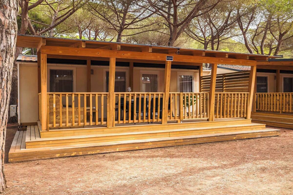 Une cabane en bois avec une véranda, une enseigne portant le numéro « M1809 », et une vue sur des arbres en arrière-plan.