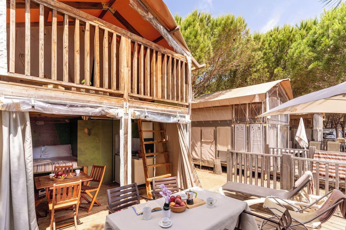 Un bâtiment en bois doté d’un balcon, d’un coin repas avec des chaises et une table, et d’un espace extérieur couvert avec des parasols.