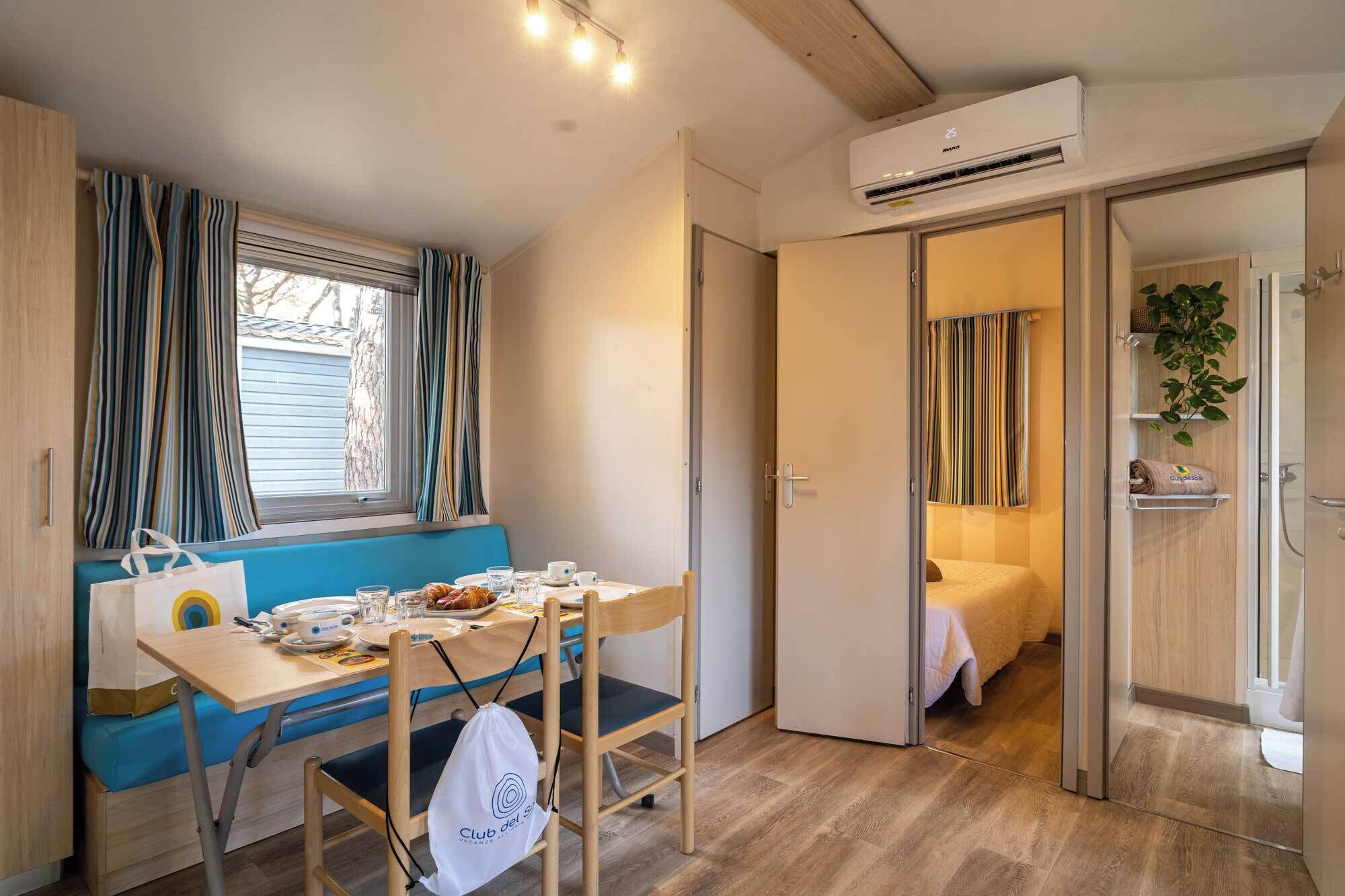 Una habitación compacta con mesa de comedor, sillas, una banca, aire acondicionado y una puerta que da a un baño.
