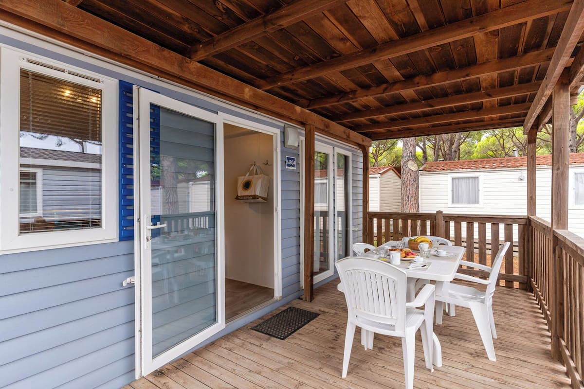 Un espace extérieur abrité, doté d’une table et de chaises, d’une terrasse en bois et d’une porte-fenêtre coulissante donnant sur une pièce.