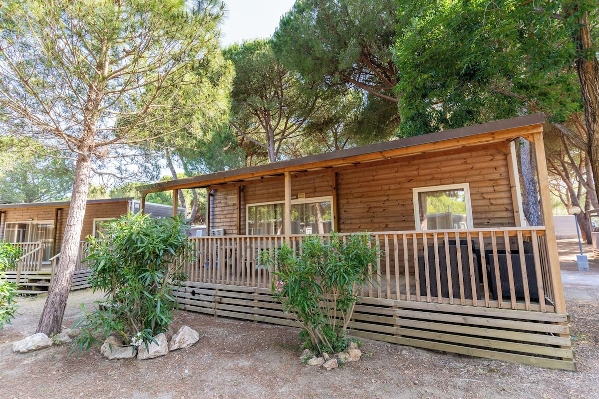 Une cabane en bois dotée d’un balcon, entourée d’arbres et bordée d’un chemin de gravier.
