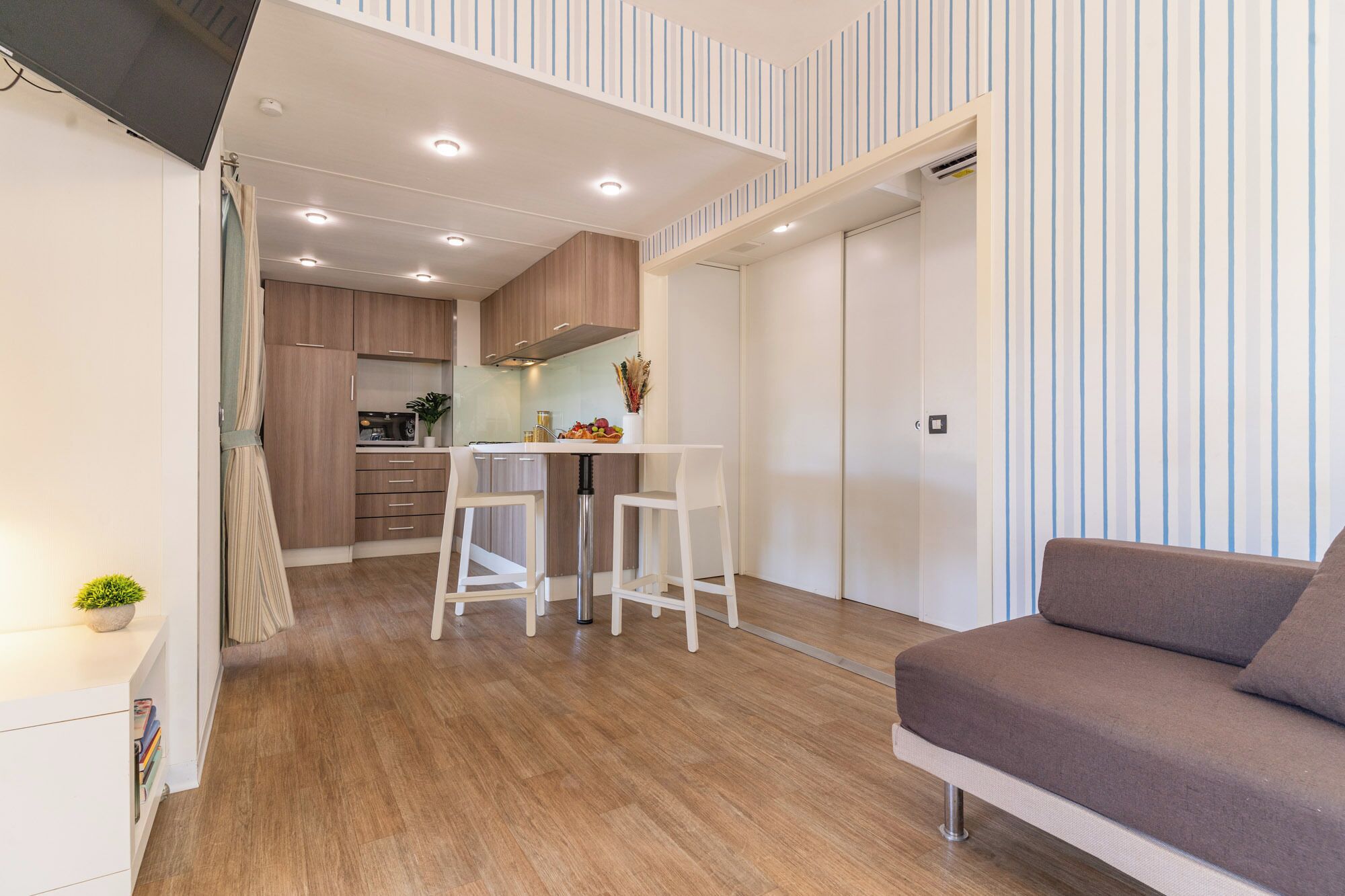 A modern kitchen with a dining area, a sofa, and a staircase leading to an upper level.