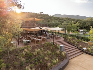 An outdoor dining area with tables and chairs, surrounded by plants and a view of hills. - Club del Sole Stella del Mare Family Collection. (Castiglione della Pescaia)