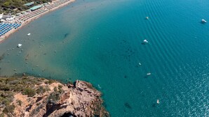 An aerial view of a coastal area with a beach, boats, and a rocky cliff.