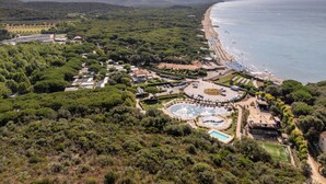 An aerial view of a coastal resort with a beach, swimming pools, and a tennis court.
