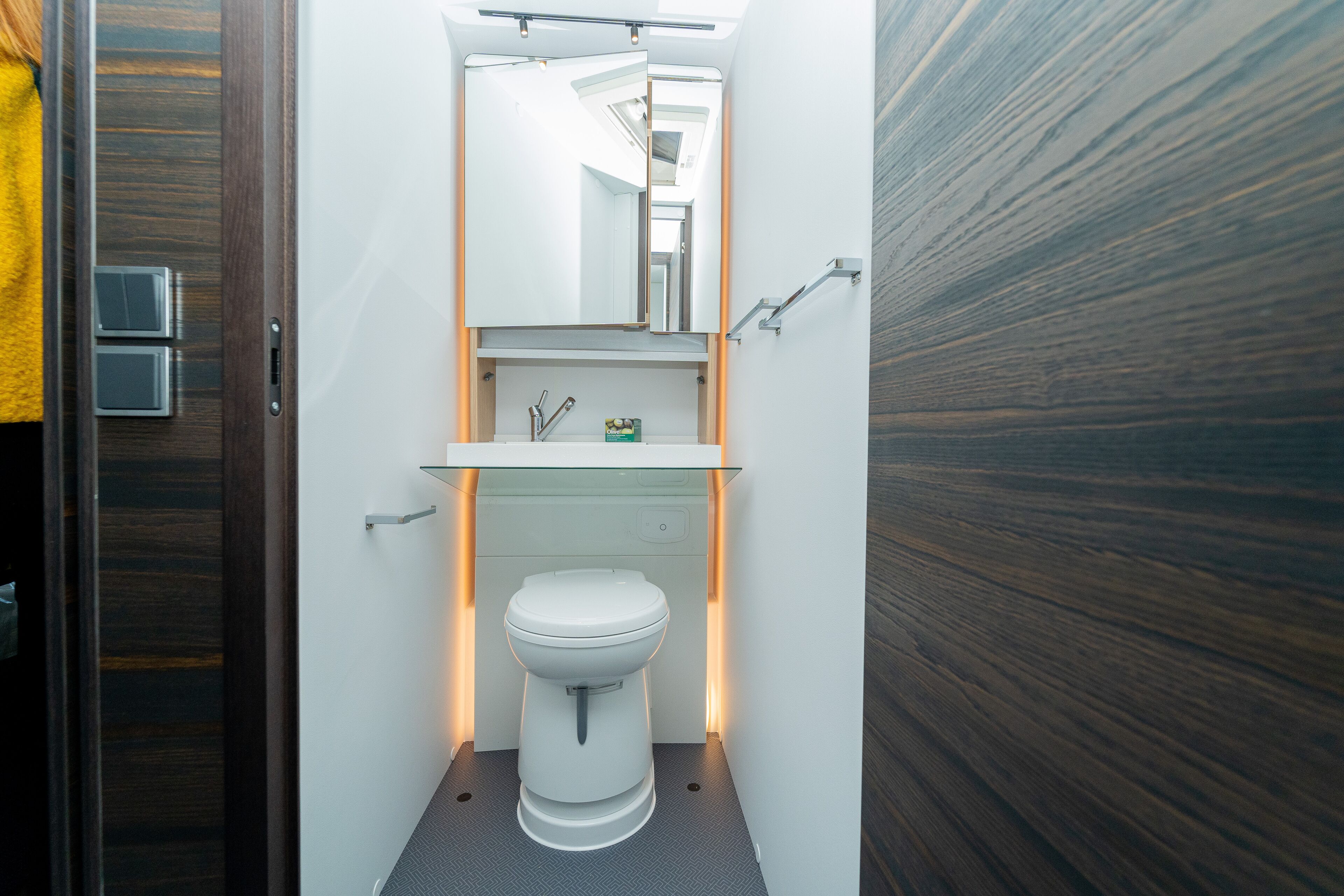 A compact bathroom with a white toilet, a glass sink, and a mirror above.