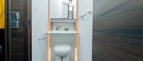 A compact bathroom with a white toilet, a glass sink, and a mirror above.