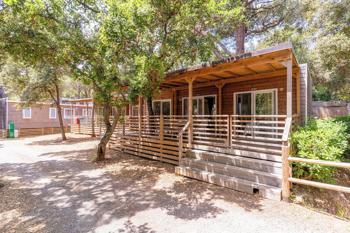A rustic cabin with a porch, wooden railings, and a gravel ground.