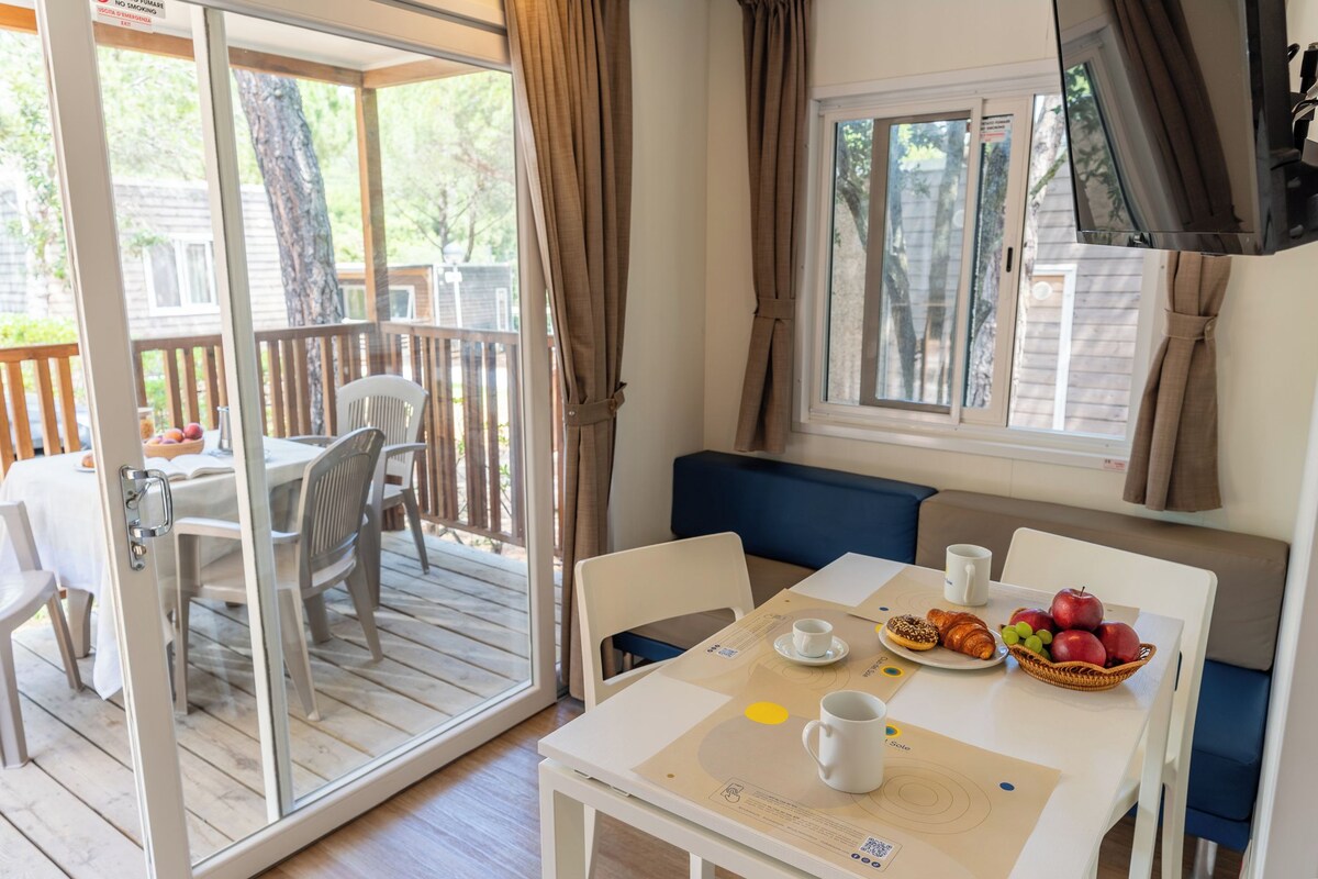 A dining area with a table set for two, a bench, and a window with curtains.
