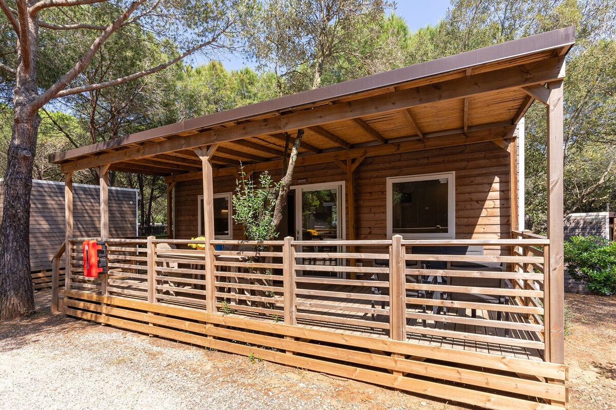 A wooden cabin with a covered porch, a fenced area, and a gravel ground.