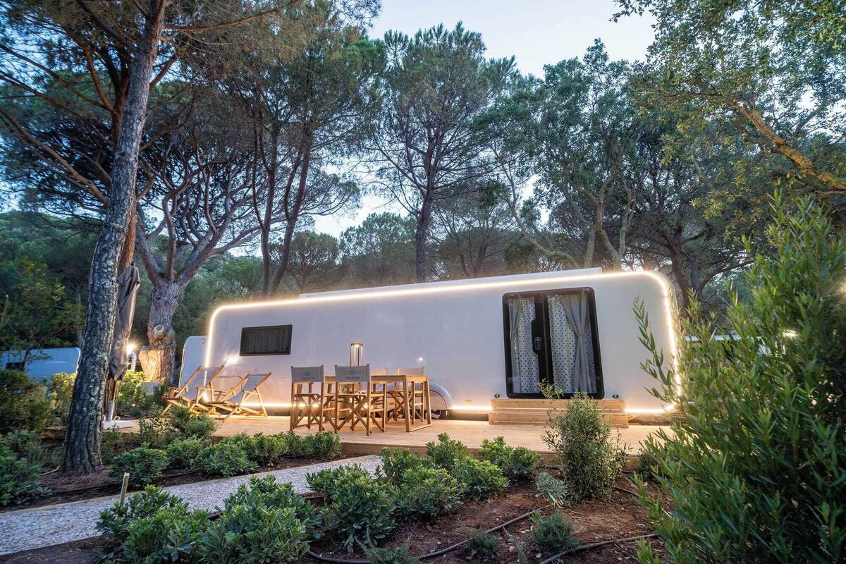 A modern RV with a covered patio area, outdoor seating, and a garden.