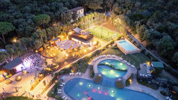 An aerial view of a resort with a swimming pool, outdoor seating areas, and a tennis court.