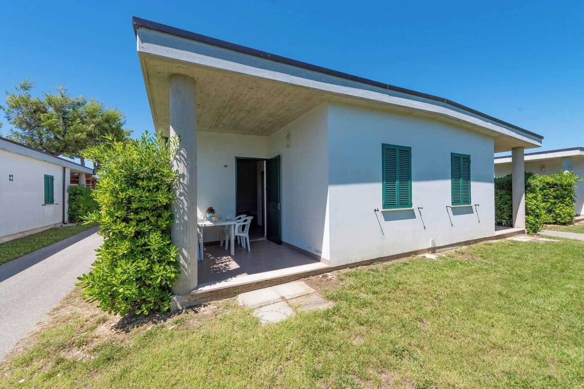 Un edificio a un piano con portico coperto, una porta e un piccolo tavolo con sedie.