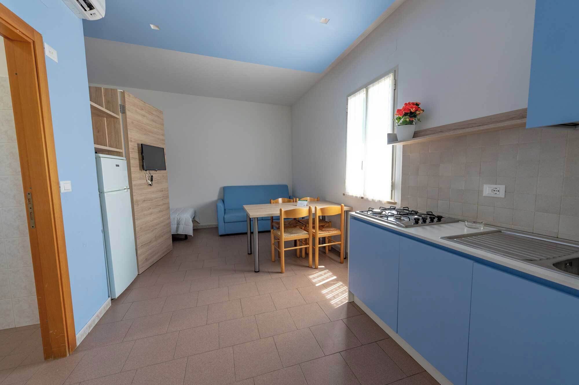 Een kleine keuken met een eethoek, een blauwe bank en een televisie.