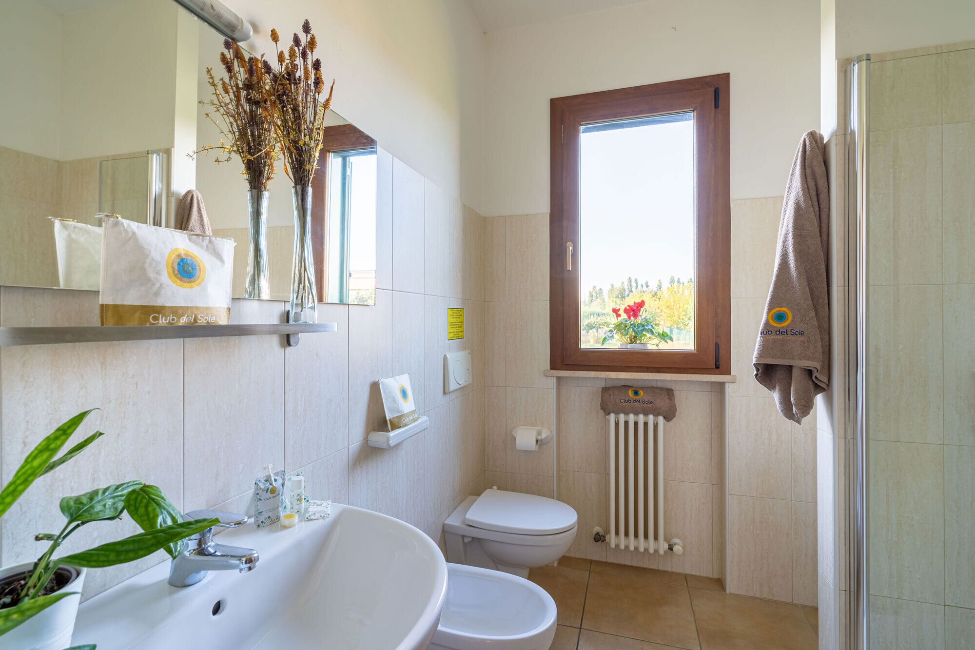 A bathroom with a sink, toilet, and shower. There are decorative plants and a towel hanging on the wall.