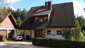 A two-story house with a sloped roof, a garage, and a car parked in front. - Tannehüsle large - quiet, with a south-facing view (St. Märgen)