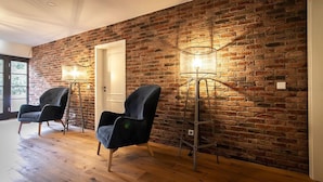 Una habitación con una pared de ladrillo, dos sillas negras y una lámpara de pie alta.