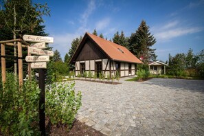A traditional half-timbered building with a tiled roof, surrounded by a cobblestone driveway and greenery.