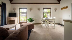 Amplia sala de estar con techo alto, televisor, mesa de comedor con sillas y una planta.