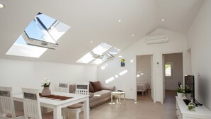 A spacious living area with a high ceiling, skylights, a dining table with chairs, a sofa, and a TV on a stand.