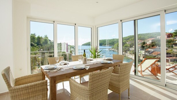 A dining area with a table set for four, large windows, and a view of a lake and buildings.
