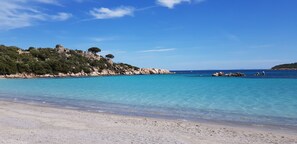 A beach with clear turquoise water, rocky cliffs, and sparse vegetation.