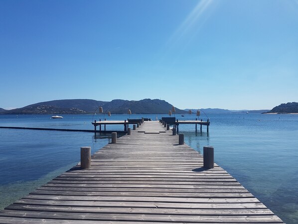 A wooden pier extending into calm waters with clear skies and distant hills.