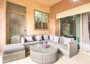 A modern living room with a sectional sofa, a round wicker coffee table, and a glass door leading to a balcony. - Splendid apartment in Prestigia Corail 4675 (Marrakech)